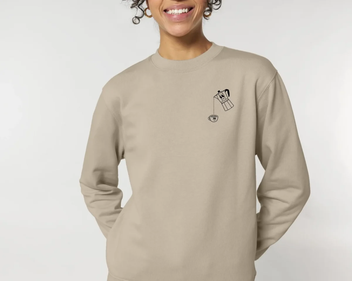 Mujer sonriente con sudadera beige y diseño divertido, luciendo estilo casual y moderno.