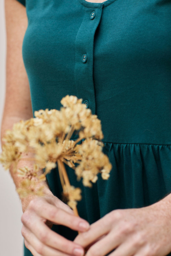 Mujer con vestido teal sosteniendo flores secas, capturando belleza y elegancia natural.