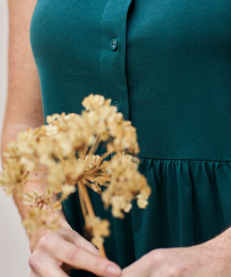 Mujer con vestido teal sosteniendo flores secas, capturando belleza y elegancia natural.