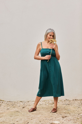 Mujer elegante con vestido verde y flores secas, irradiando serenidad y conexión con la naturaleza.