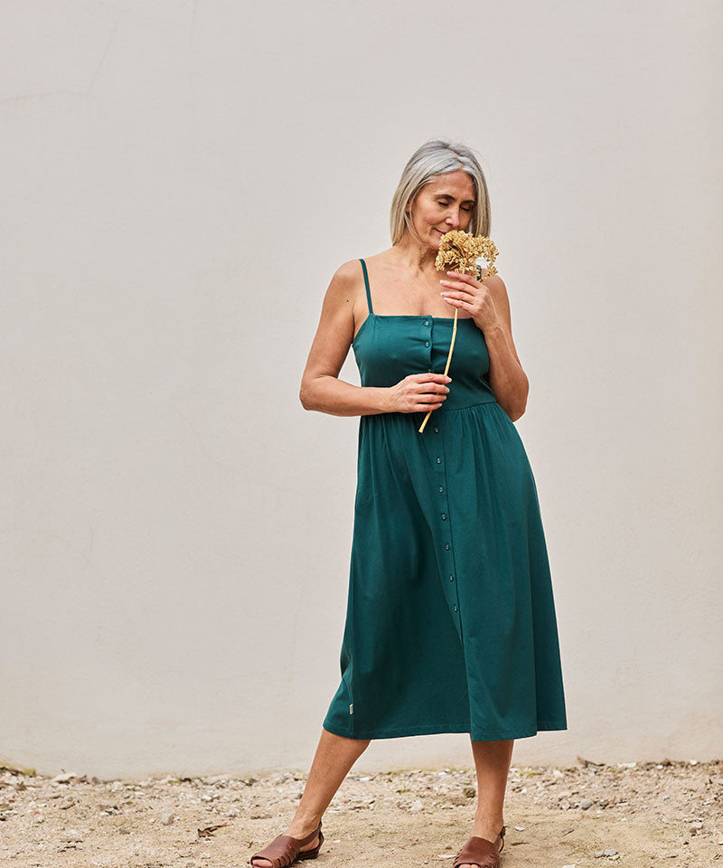 Mujer elegante con vestido verde y flores secas, irradiando serenidad y conexión con la naturaleza.