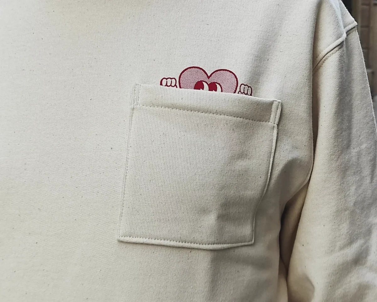 Sudadera beige con bolsillo de corazón, cómoda y perfecta para un estilo casual y divertido.