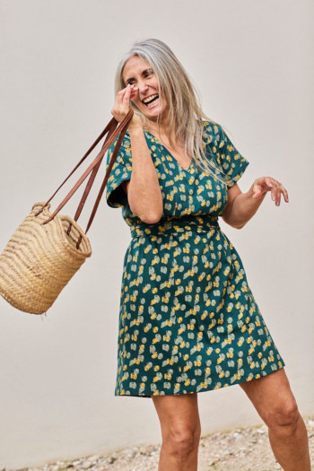 Mujer alegre con vestido floral y bolso de paja, posando con energía y estilo.