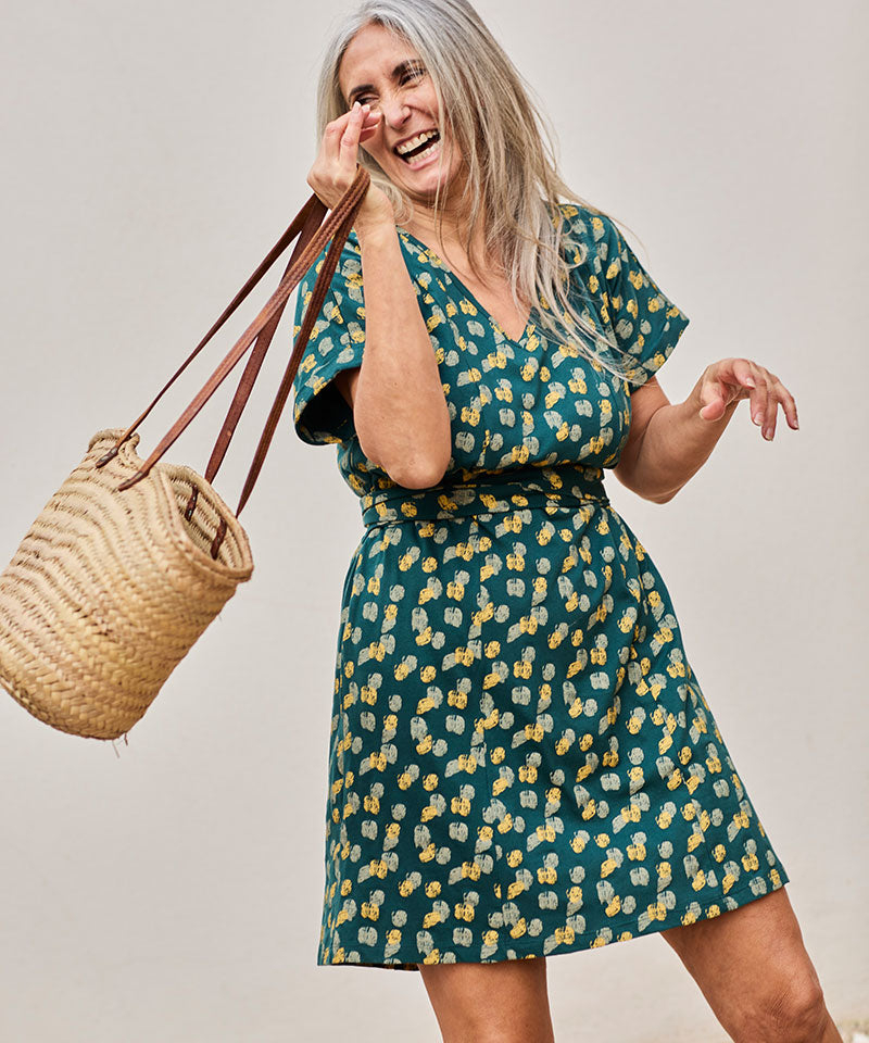 Mujer alegre con vestido floral y bolso de paja, posando con energía y estilo.