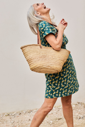 Mujer alegre con vestido verde y cabello plateado, disfrutando de un día soleado.