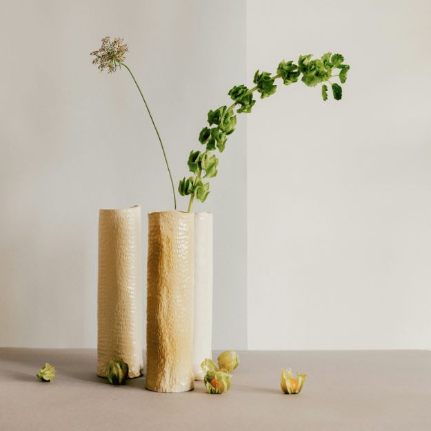 Arreglos florales minimalistas en jarrones contemporáneos sobre fondo neutro, con pétalos caídos.