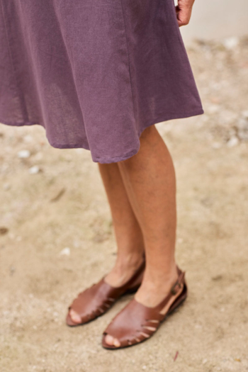 Mujer con vestido morado y sandalias de cuero en un entorno natural relajante.