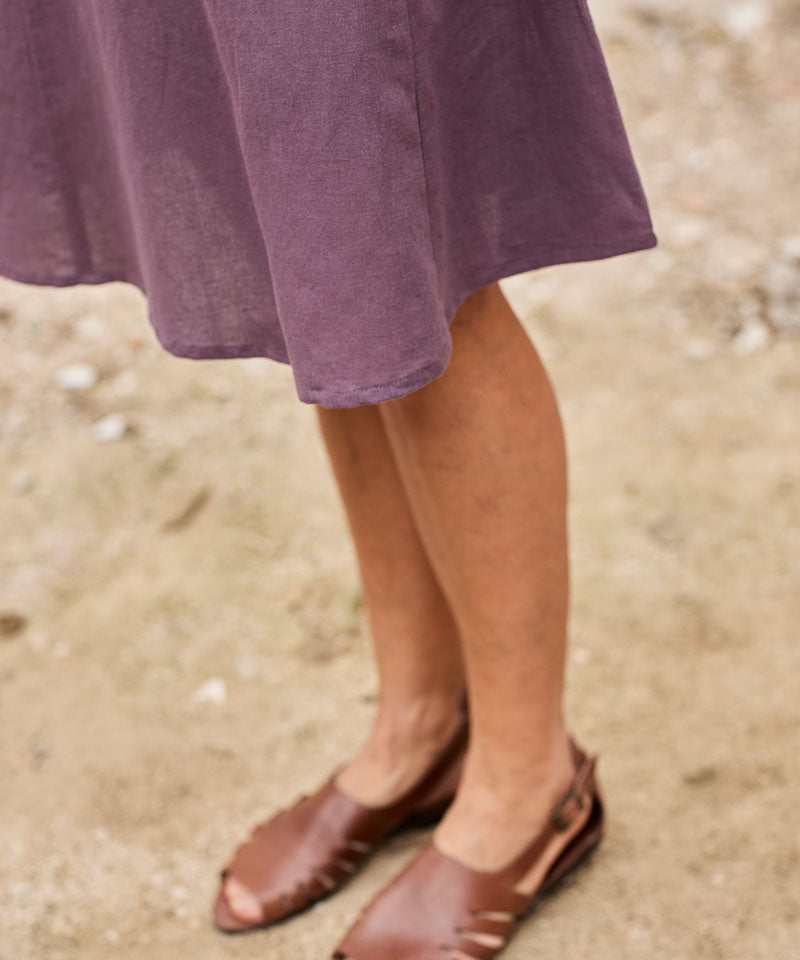 Mujer con vestido morado y sandalias de cuero en un entorno natural relajante.