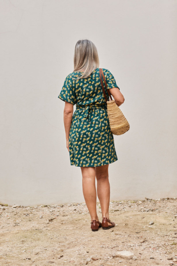 Mujer elegante con vestido verde en un ambiente exterior relajante y cálido.