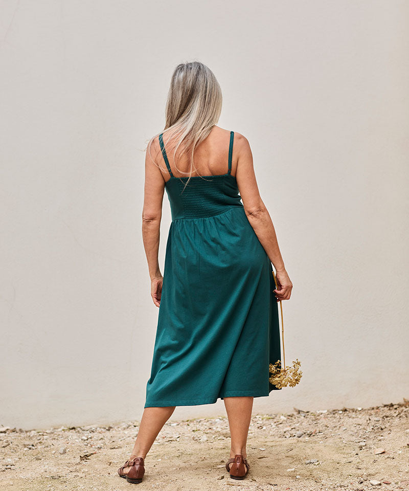 Mujer con vestido teal y ramo de flores secas, transmitiendo serenidad y elegancia.