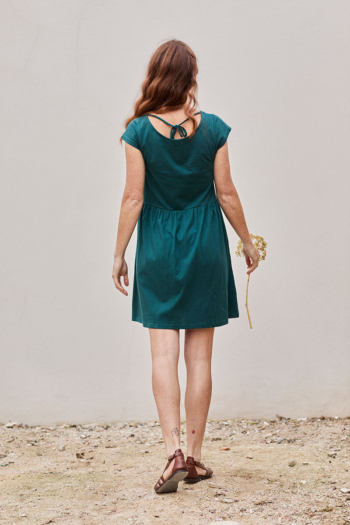 Mujer con vestido teal en un entorno natural, sosteniendo una flor, transmitiendo tranquilidad.