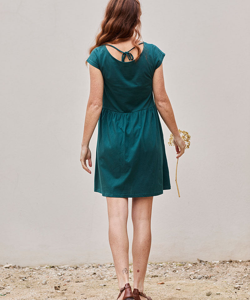 Mujer con vestido teal en un entorno natural, sosteniendo una flor, transmitiendo tranquilidad.