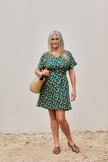 Mujer sonriente con vestido vibrante y bolso de paja en un fondo neutro.