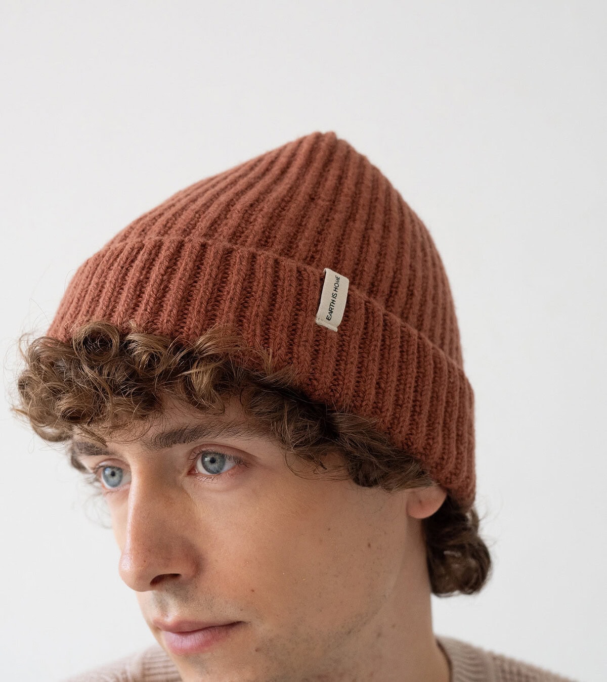 Joven con gorro acogedor, pelo rizado y mirada serena. Estilo casual y sofisticado.