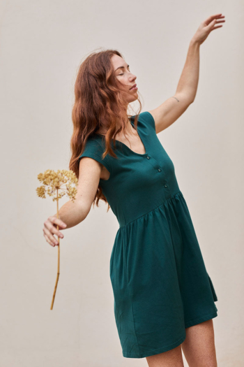 Mujer joven con vestido teal y flores secas, irradiando calma y elegancia.