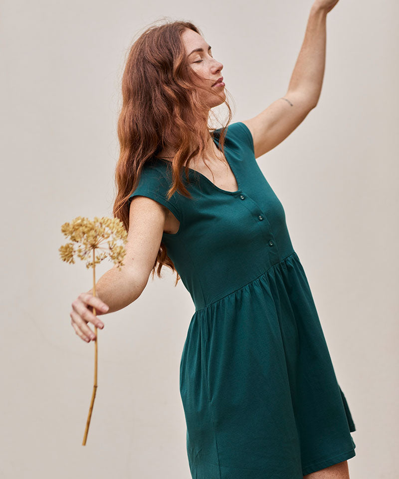 Mujer joven con vestido teal y flores secas, irradiando calma y elegancia.